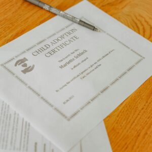 Close-up of a child adoption certificate and documents with a pen on a wooden table.